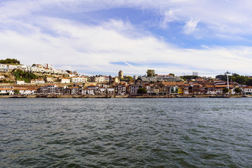 Fototapeta na wymiar Porto, Portugal. August 12, 2017: panoramic view of the south bank of the Douro River estuary with the facades of the wineries that are on its banks with a sky with few very beautiful clouds