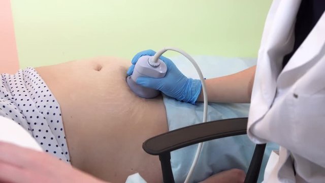 Closeup view of a pregnant womans belly while getting ultrasound scan by a male doctor