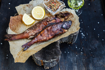 Smoked fish with lemon slices on backing paper on dark wooden smoking background, top view, copy space
