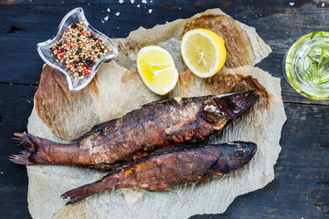 Smoked fish with lemon slices on backing paper on dark wooden smoking background, top view, copy space
