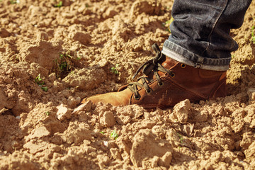 Man is walking on plowed field. Man's leg in a shoe on brown soil