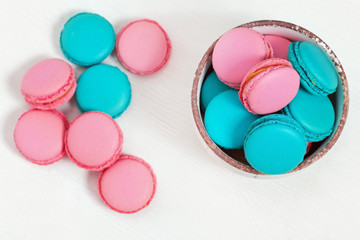 Pink and blue almond cookies macarons in plate on white wooden table with copy space. Crispy sweet dessert. Top view.