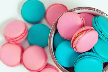 Sweet colorful macaroons close up in bowl on wooden white table. Top view. French pink and blue macaroons.