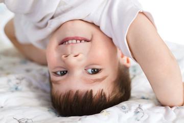 Obraz na płótnie Canvas Close up shot of handsome smiling little boy stands on head, being glad, has fun after good sleep, has pleasant smile on face, has appealing appearance, healthy soft skin. Children and entertainment