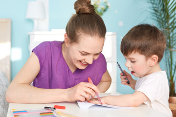 Children, art and education concept. Smiling lovely young mother draws palm print of her son on...