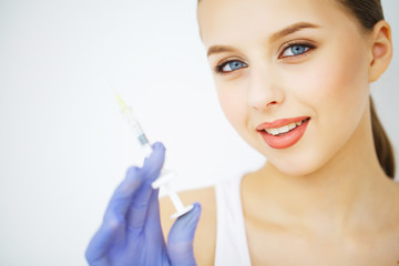 Close up of hands of cosmetologist making botox injection in female lips. She is holding syringe. The young beautiful woman is receiving procedure with enjoyment