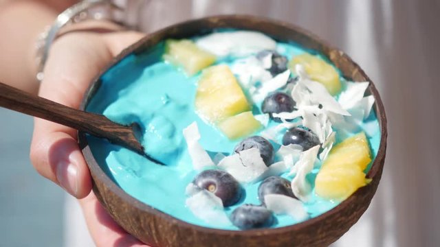 hands holding blue majik smoothie bowl approaching camera lens