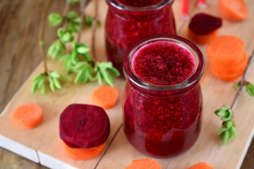 Red vegetable smoothie made of carrot and beetroot in glass jars on wooden background