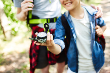 Young boy scout his companion walking after compass arrow while looking for the camp in the forest