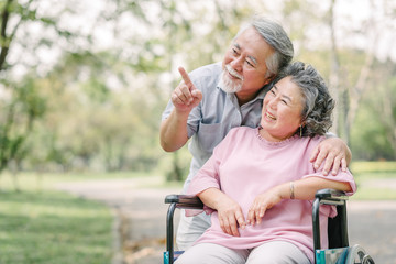 Happy Asian senior couple smiling outside while sitting in wheel chair