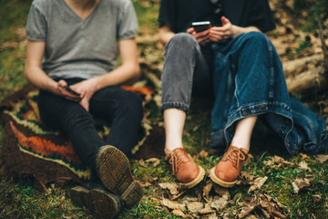 couple is sitting on the grass with shoes looking at cellphones