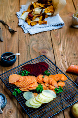 Healthy vegetable chips mix with spices in paper on old rustic wooden table, diet, cooking, vegetarian and clean eating concept, closeup