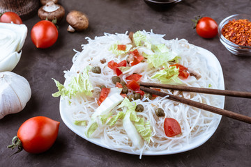 Rice noodles with vegetables, capers and soy sauce in the ceramic plate  on dark background.