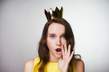 A young blue-eyed girl in a yellow dress looks surprised, a golden crown on her head