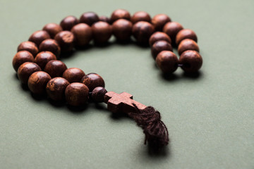 Wooden  rosary and cross on green background.