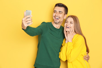 Young lovely couple taking selfie against color background