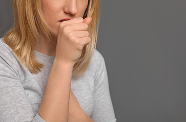 Young woman coughing on grey background