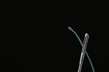 Needle with sewing thread on black background, closeup