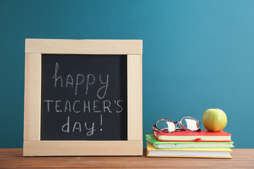 Little blackboard with inscription HAPPY TEACHER'S DAY, notebooks and eyeglasses on table