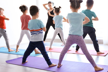 Fototapeta na wymiar Little children and their teacher practicing yoga in gym