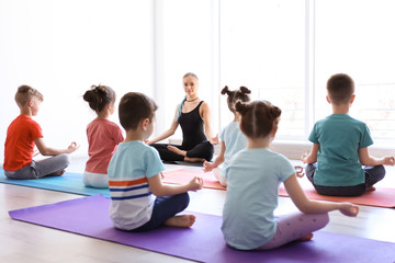 Little children and their teacher practicing yoga in gym
