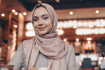 cute arabic girl with a headscarf sitting in a cozy oriental cafe, smiling and looking at the camera
