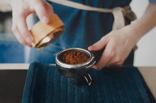 The Barista girl prepares coffee, filling the coffeemaker with ground coffee and took tamper for pressing coffee. Side view with copy space for your text.