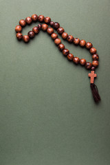 Wooden  rosary and cross on green background.