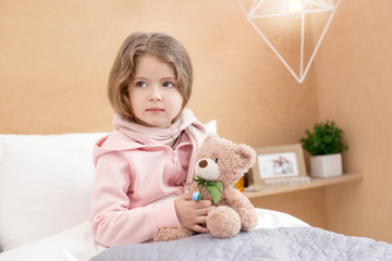 Having a rest. Charming little girl sitting on her bed and holding her toy