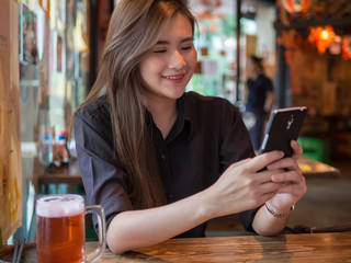 Happy young woman eating sushi in a restaurant and using mobile phone