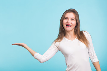 Fototapeta premium Young woman pointing at copy space on blue background
