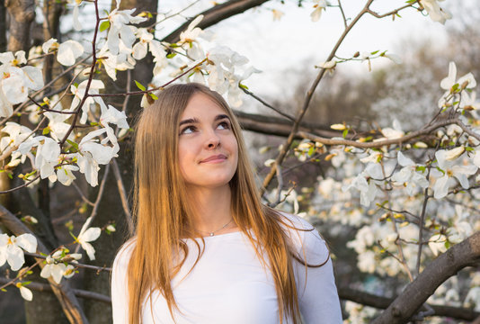 Young beautiful girl looks up on white magnolia background
