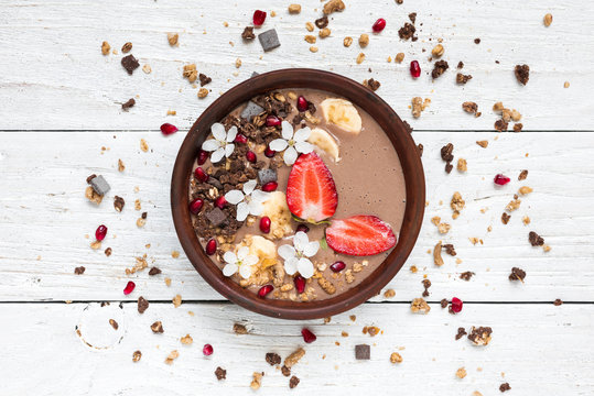 cocoa banana protein smoothie bowl with chocolate granola, strawberry and pomegranate seeds decorated with flowers