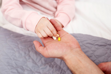Recovery. Little sick girl having a flu and taking pills from her daddys palm