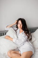 Naklejka premium sexy young brunette woman wearing a white shirt on the bed at home. Girl's morning