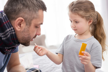 Your medicine. Adorable little girl taking care of her sick daddy and giving him a pill