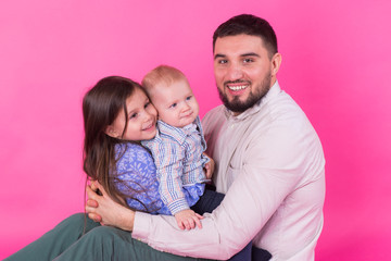 handsome father carrying his little daughter and baby son on pink background