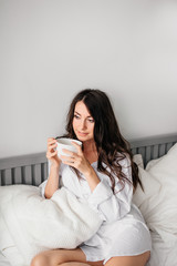 Portrait of beautiful young woman drinking coffee on bed at home 