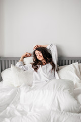 sexy young brunette woman wearing a white shirt on the bed at home. Girl's morning
