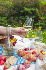 picnic basket and food. A bottle of wine and a glass in a woman's hand. Romanica. Green meadow with flowers. Spring in the Netherlands. Holidays. Top view. Place for text