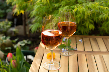 Two cold rose wine glasses served on outdoor terrace in garden with flowers in sunny day