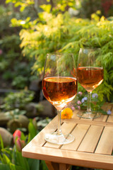 Two cold rose wine glasses served on outdoor terrace in garden with flowers in sunny day