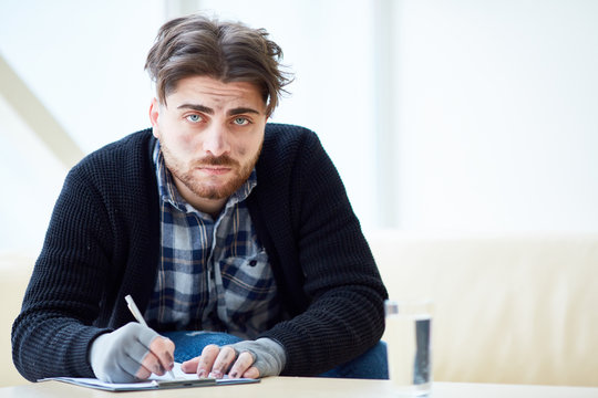 Dirty homeless man looking at camera while filling in papers in the center of social support