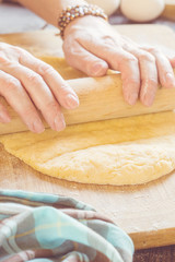 Woman kneading a dough whith rolling pin on a table