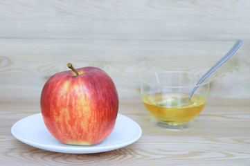 A red and yellow apple on a white plate and honey in a croissant with a spoon on a wooden background