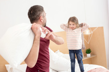 Joy. Alert adorable daughter spending with her daddy and having a pillow battle