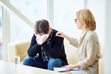 Psychologist giving advice to her addicted patient crying in handkerchief while sharing his...