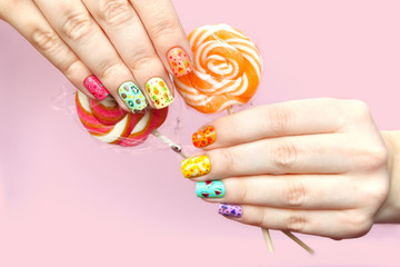 Woman's hands with colorful fruit manicure holding lolly pops. Pink background.
