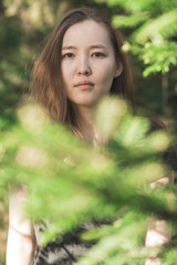 Naklejka premium Beautiful young Mongolian female in the green forest looking through trees. Asian girl relaxing in nature.