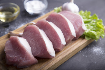 Raw slice pork on wooden board with spices and olive oil